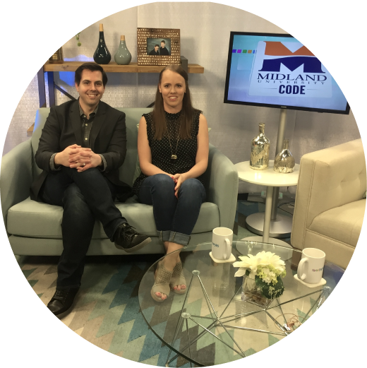 Becca and a colleague seated on a couch in a TV studio, a screen behind them showing the Midland University Code logo