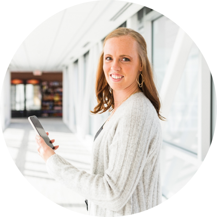 Becca Kroese, smiling, holding a phone in a sunlit building